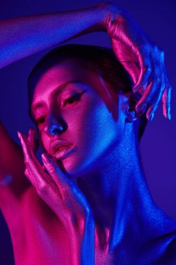 Renkli mavi ve pembe ışıkta zarif poz veren parlak gümüş tenli güzel bir mankenin stüdyo fotoğrafı. Güzellik ve kozmetik konsepti. Vücut boyama. Mavi arkaplan.