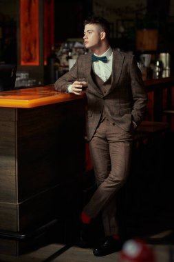 Şık takım elbiseli çekici bir esmer adam bir restoranda viski içerek barda dinleniyor. İş adamı. Lüks yaşam tarzı.