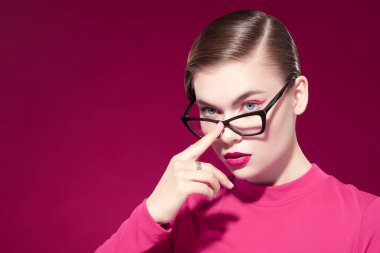 Parlak makyajlı ve fuşya arka planında zarif gözlüklü güzel bir kadının stüdyo portresi. Makyaj ve makyaj malzemeleri. Zarif gözlük stili. 