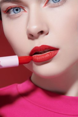Güzellik kızı. Sevimli kırmızı renk. Parlak makyajlı güzel bir kız modelin portresi kırmızı arka planda muhteşem bir kırmızı ruj sürüyor. Yakın çekim..
