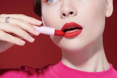 Sevimli kırmızı renk. Güzel bir kız modelin parlak kırmızı ruj sürerken çekilmiş bir fotoğrafı. Yakın çekim. Makyaj ve kozmetik. 
