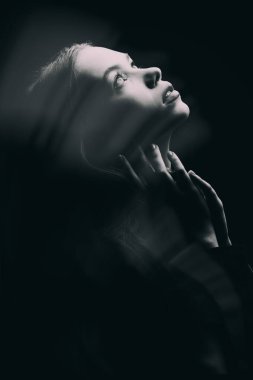 Siyah arka planda bir kızın umut dolu bir şekilde ışığa bakışının siyah beyaz görüntüsü. Psikolojik portre.