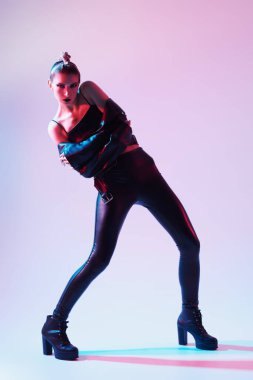 Moda ve rock tarzı. Siyah deri kıyafetler ve siyah çizmeler giymiş agresif bir mankenin tam boy portresi. Açık pembe stüdyo arka planında karışık ışıklandırma.