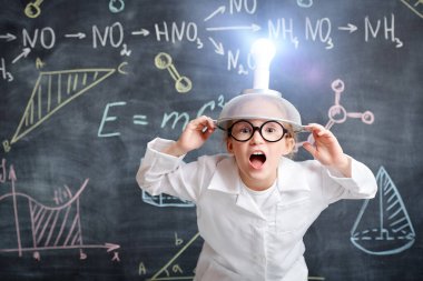 Beyaz gömlekli ve gözlüklü komik küçük bir kız kafasında garip bir icatla kimyasal formüller ve diyagramlarla tahtaya dayanıyor. Eğitici kavram. 