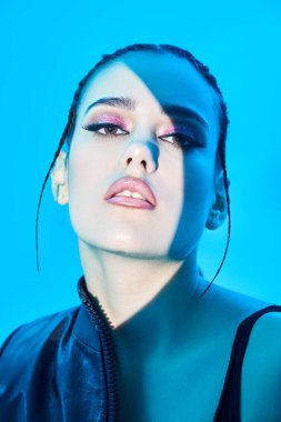 Parlak akşam makyajı ve mavi bir arka planda poz veren parlak ışık demeti olan şehvetli esmer bir kızın portresi. Stüdyo çekimi. Güzellik, makyaj ve kozmetik konsepti. 