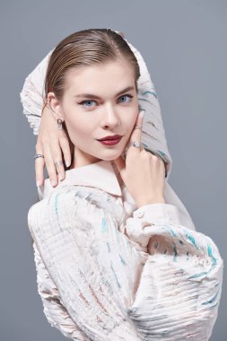 Moda modası. Muhteşem genç kadın manken geniş kollu abartılı bej bluzla poz veriyor. Makyaj ve mücevher. Gri arkaplan.