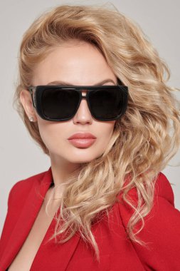 Kıvırcık sarı saçlı, şık kırmızı ceketli ve şık siyah gözlüklü güzel bir genç bayan. Stüdyo portresi. Güzellik, moda. Gözlük stili.