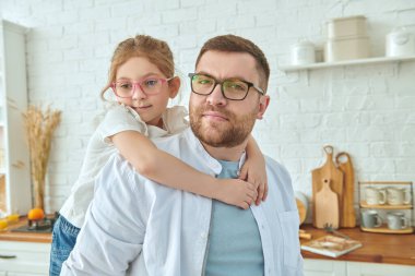 Modern bir mutfakta kızını sırtında taşıyan bir babanın portresi. Modern iç mekan, mutfak mobilyası. Mutlu aile. 