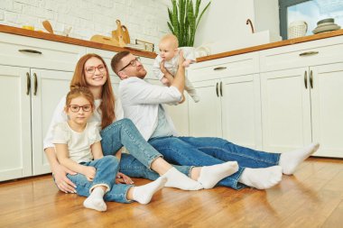 Mutfakta yerde neşeyle oturan mutlu aile portresi. Modern iç mekan, mutfak için mobilya. Aile.