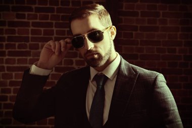 Şık takım elbiseli ve siyah güneş gözlüklü yakışıklı bir adamın portresi. Erkek modası.