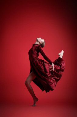 Dans sanatı, modern bale. Kırmızı kadife elbiseli güzel balerin kız stüdyoda kırmızı arka planda ifade ile dans ediyor. Tam boy portre.
