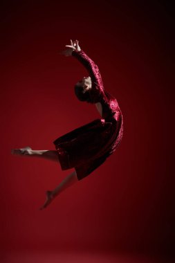 - Bale. Kırmızı kadife elbiseli güzel balerin kız atlayışta uçuyor. Tam boy stüdyo resmi..