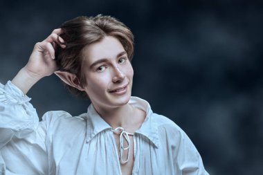 Karanlık bir yerde gülümseyen ve başını kaşıyan neşeli bir elf çocuğunun portresi. Fantezi. Peri masalı, sihir. 