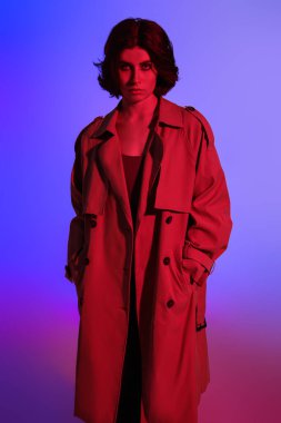 Stüdyoda çok renkli arka planda kırmızı ışıklı şık bir yağmurlukla poz veren güzel bir manken. Moda fotoğrafı.. 