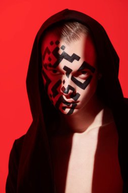 Yüzüne QR kodu çizilmiş genç bir adamın sanat portresi. Bir ışık demeti tarafından aydınlatılan kameraya bakıyor. Kırmızı arka plan. QR kod kavramı, koronavirüse karşı aşı. 