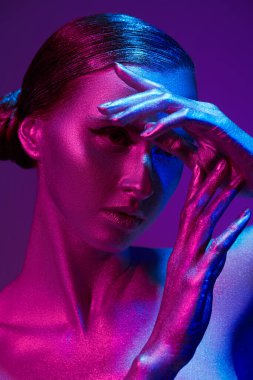 Güzel, kadınsı bir modelin sanat portresi. Mor bir arka planda parlak gümüş renkli, neon mavi ve kırmızı bir ten. Güzellik ve kozmetik konsepti. Vücut boyası. 