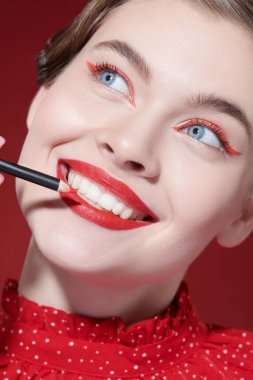 Makyaj ve makyaj malzemeleri. Parlak kırmızı rujlu güzel bir kız modelin portresi dudaklarını kaplamak için kırmızı bir dudak kalemi sürüyor. Yakın çekim..