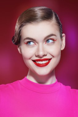 Parlak kırmızı rujlu, kırmızı okları olan güzel bir sarışın kız. Kırmızı bir arka planda ışıltılı bir şekilde gülümsüyor. Makyaj ve makyaj malzemeleri. Güzellik konsepti.