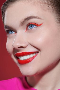 Kozmetik ve makyaj malzemeleri. Parlak kırmızı rujlu güzel bir sarışın kız ve kırmızı arka planda büyüleyici bir şekilde gülümseyen kırmızı okları var. Güzellik konsepti.