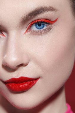 Makyaj ve makyaj malzemeleri. Kırmızı arka planda parlak kırmızı rujlu ve kırmızı oklu güzel bir sarışının yakın plan fotoğrafı. Güzellik konsepti.