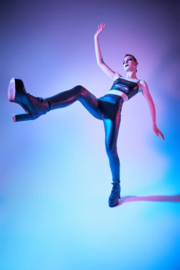 Dar siyah deri kıyafetler ve yüksek topuklu siyah çizmeler içinde uzun bacaklı ince bir manken. Aydınlatmalı stüdyo çekimi. Rock tarzı moda.. 