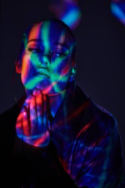 Sanal gerçeklik kavramı. Siyah deri ceketli, parlak makyajlı çekici bir esmer kızın portresi. Renkli lazer ışınlarıyla dolu karanlık bir yerde duruyor.. 