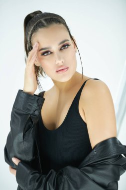 The concept of makeup and cosmetics. Portrait of a beautiful brunette girl with bright evening makeup posing in a stylish top and leather jacket. Studio shot on a white background.