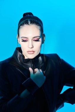 Çekici bir esmer kız modelinin portresi. Yüzüne ışık düşen mavi bir arka planda şık siyah deri ceketle poz veriyor. Moda ve güzellik çekimi. 