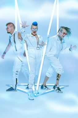 Gelecekçi mekan ve cybepunk tarzı. Üç karizmatik müzisyen neon ışıklar arasında beyaz konser kostümleri içinde poz veriyor. Performans, gösteri. Tam boy portre.