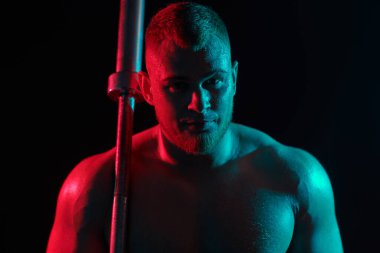Yakışıklı bir erkek halterci, koyu renk bir arka planda halterle egzersiz yapar. Kırmızı ve mavi ışıklandırmalı. Profesyonel spor. Ağırlık kaldırma. 