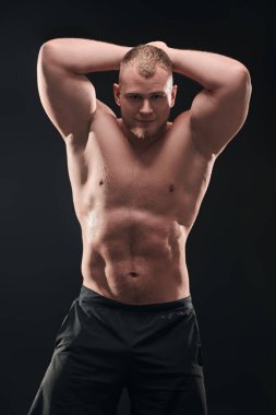 Siyah arka planda poz veren kaslı vücutlu yakışıklı, kendine güvenen genç bir adamın stüdyo fotoğrafı. Profesyonel spor, vücut geliştirme.. 