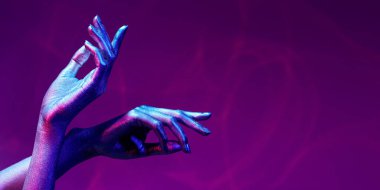 Photo of graceful thin hands with sparkling silvery skin in bright neon blue and pink lighting. Body painting, body art. Glitter makeup. Beauty industry, cosmetology. Copy space.