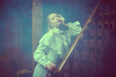 Beyaz dantel elbiseli güzel bir aristokrat kadın klasik klasik bir dairede, açık bir sis ile çevrili merdivenlerde duruyor. Viktorya tarzı. Tarihi roman..