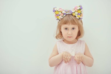 4 yaşında, güzel bir kızın portresi. Sarı saçlı, pembe elbiseli, saçı kenarlı ve önünde ellerini sıkıca tutan çiçeklerle. Beyaz stüdyo geçmişi. Çocuk modası.