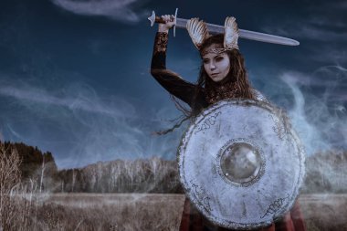 Efsanevi fantezi. İlahi kadın savaşçı Valkyrie savaş meydanında elinde bir kılıç ve kalkanla karanlıkta savaşıyor. İskandinav mitolojisi. Boşluğu kopyala.