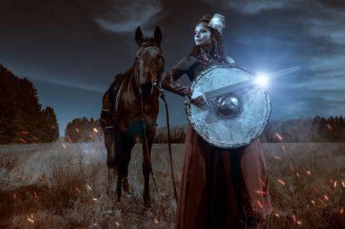 Cesur ve güzel kadın savaşçı Valkyrie savaş alanında savaş atının yanında elinde bir kılıç ve kalkanla duruyor. İskandinav mitolojisi. Efsanevi fantezi.