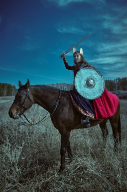 Cesur ve güzel kadın savaşçı Valkyrie karanlık zamanlarda savaş atının üzerinde oturan bir kılıç ve kalkanla savaşıyor. İskandinav mitolojisi. Efsanevi fantezi.