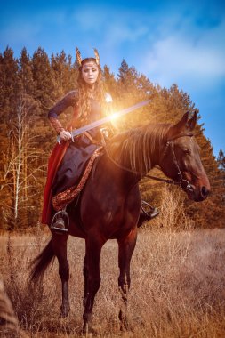 Güzel bir savaşçı Valkyrie, elinde kılıçla bir savaş atına binip savaşa hazırlanıyor. İskandinav mitolojisi. Fantezi.