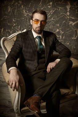 Lüks bir yaşam tarzı. Zarif klasik takım elbiseli ve güneş gözlüklü saygıdeğer bir adam dairedeki eski bir koltukta oturuyor. Erkek güzelliği, moda.