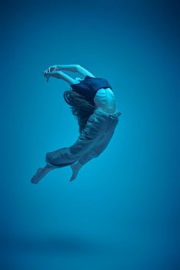 Dans ifadesi. Modern balerin kız atlıyor. Çağdaş bale. Mavi ışıkta tam boy stüdyo portresi.