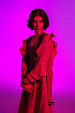 Stüdyoda, parlak pembe arka planda kırmızı ışıklı şık bir yağmurlukla poz veren güzel bir manken. Moda fotoğrafı.. 