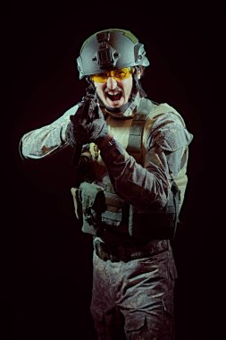 Koruyucu Savaş Üniformalı cesur bir asker öfkeyle bağırıyor ve siyah arka planda otomatik bir silahla nişan alıyor. Savaş ve askeri kavram. 