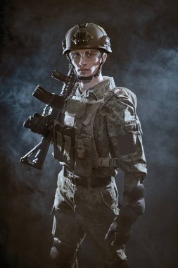 Koruyucu Savaş Üniformalı cesur bir asker karanlıkta dumanla kaplı bir saldırı tüfeğiyle ayakta duruyor. Savaş ve askeri kavram.