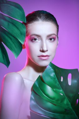 Yumuşak pembe makyajlı çekici esmer kadın yeşil tropikal yaprakların arkasında duruyor. Orman fotoshop 'u. Spa, cilt bakımı ve kozmetik ürünleri. 