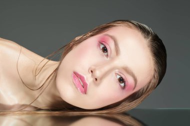 Açık pembe makyajlı güzel model kadın yansıtıcı yüzeyde uzanan kameraya bakıyor. Stüdyo çekimi. Kadın güzelliği ve sağlığı. Kozmetik ve cilt bakımı. 