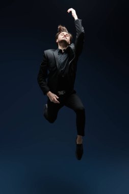 Siyah, klasik takım elbiseli bir adam atlar, özgürlüğü ve hafifliği hisseder. Koyu mavi arka planda stüdyo boy portresi. Mutluluk. Başarı ve arzu kavramı, hayaller.. 