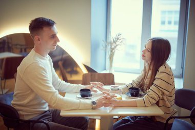 Genç ve sevgi dolu bir çift, rahat bir kafede el ele tutuşup birbirlerinin gözlerinin içine bakarak neşeyle bir masada otururlar. Aşk ve ilişki, yaşam tarzı. Aşık mutlu çift.