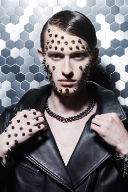 Agresif bir moda. Siyah deri ceketli ve yüzünde metal çiviler olan vahşi bir gencin portresi. Metalik teknik arkaplan.