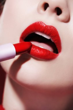 Sevimli kırmızı renk. Güzel bir kız modelin parlak kırmızı bir ruj sürerken yakın plan fotoğrafı. Makyaj ve kozmetik. 