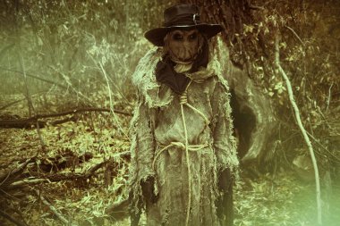 Kafasında çuval bezi ve siyah şapkası olan tüyler ürpertici bir korkuluk sık bir ormanda duruyor. Eski tarz. Cadılar Bayramı Masalları. Korku, gerilim.